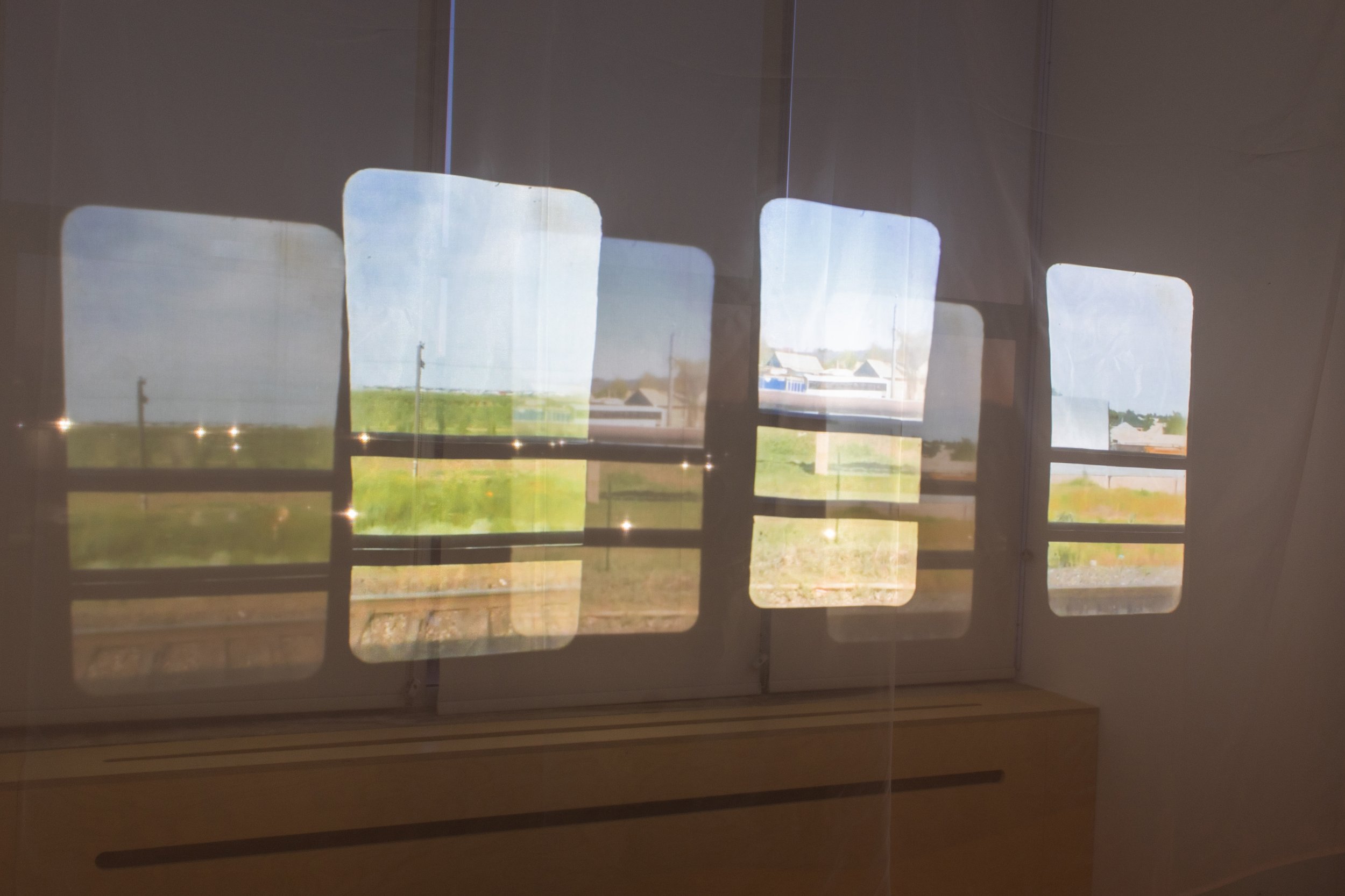 Multiple overlapping projected views through train windows showing fields, houses, and passing landscape.