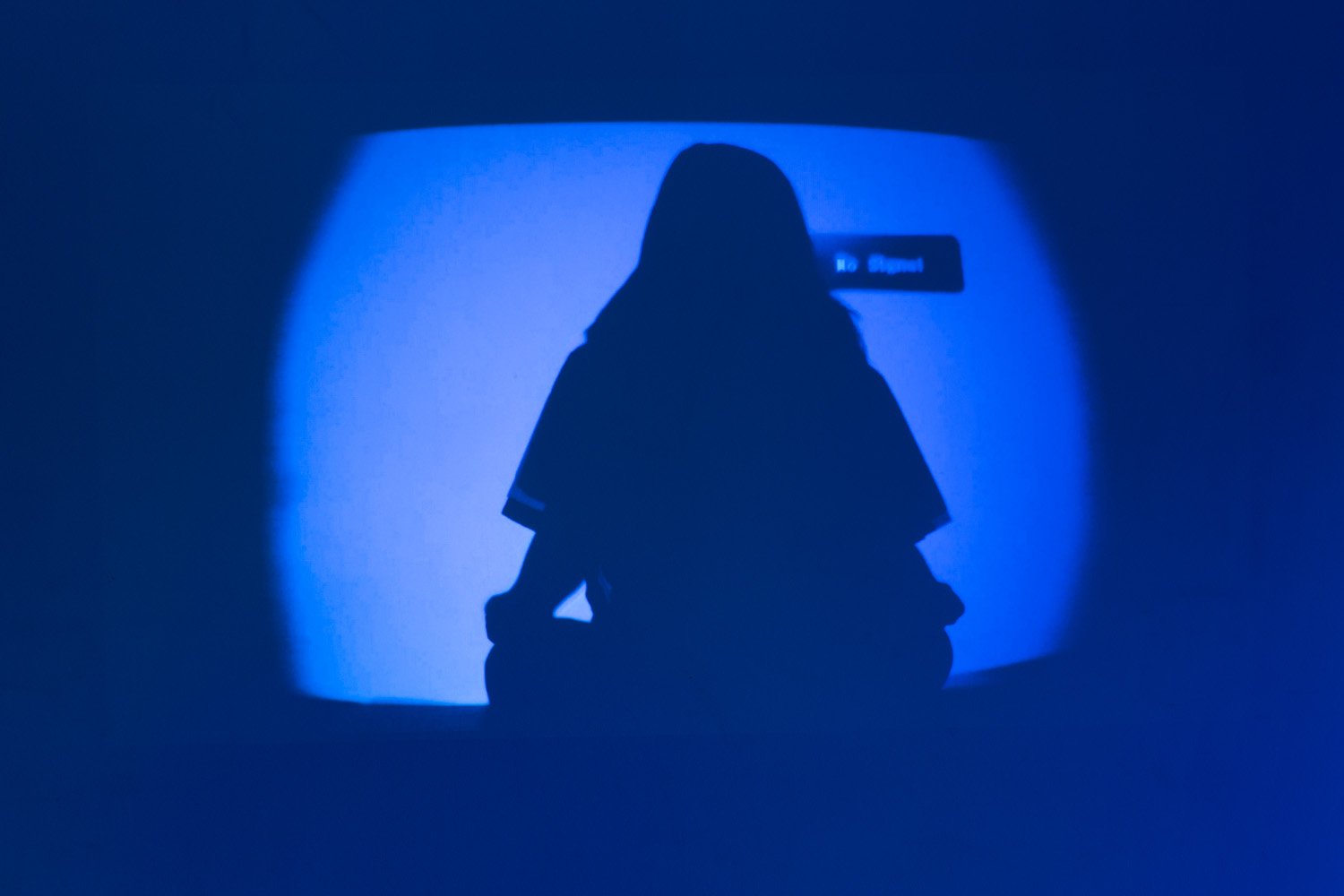 Silhouette of a seated person meditating in front of a glowing blue video projection.