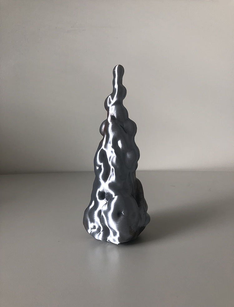 Tall metallic silver 3D-printed sculpture with irregular bulbous contours standing on a gray surface.