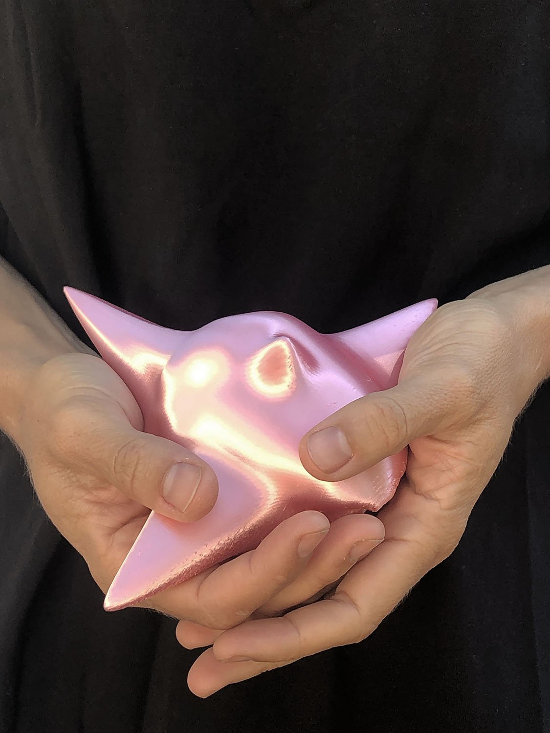 Two hands holding a glossy metallic pink 3D-printed sculpture with pointed and rounded organic forms.