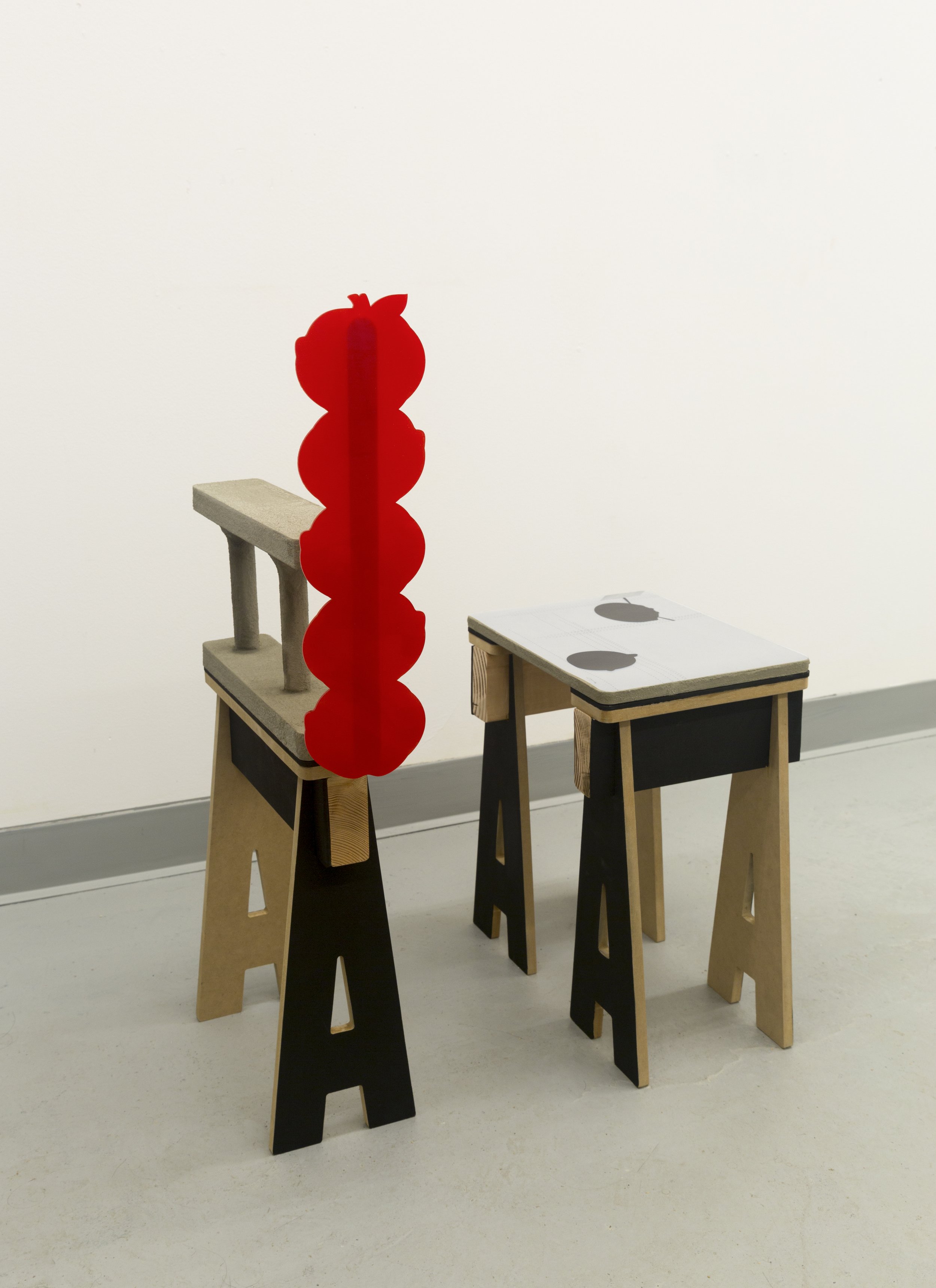Two small furniture-like sculptures beside a bright red vertical acrylic form composed of five stacked apple silhouettes.