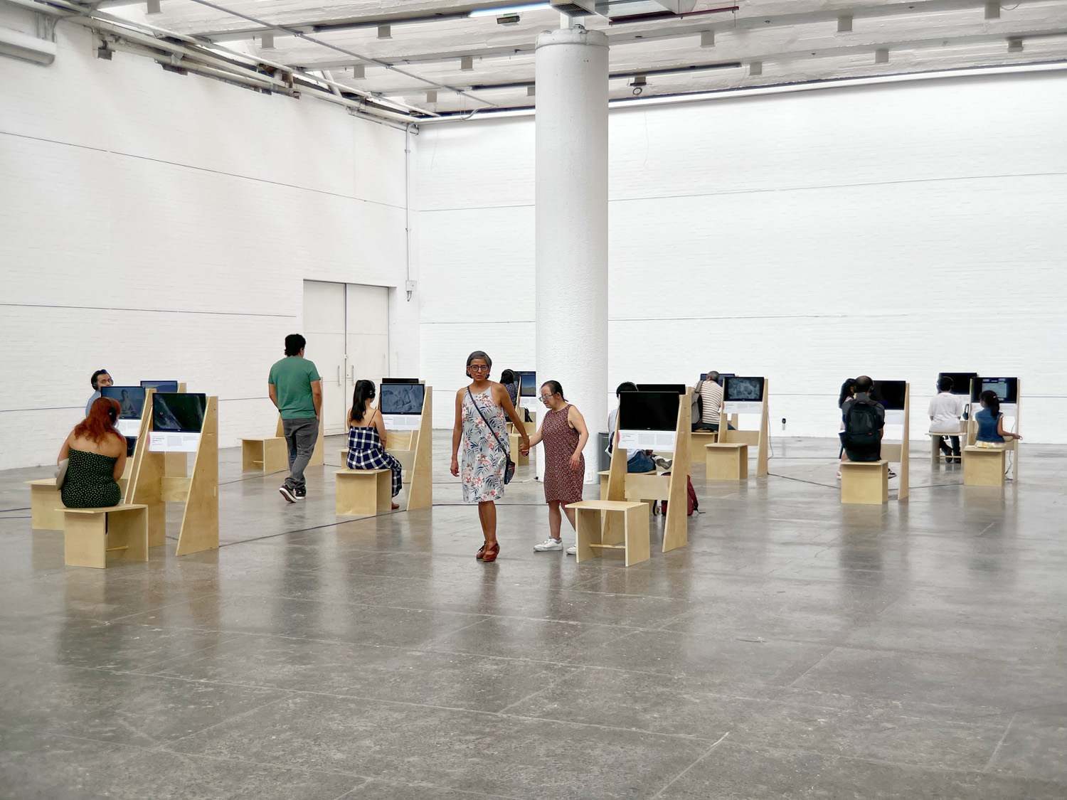 Visitors viewing Projected Ecologies, seated and standing at individual video stations throughout the gallery.